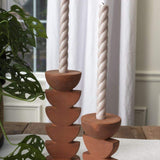 Two Cadwell Candle Holders with stacked half moon design in natural terracotta, holding twister taper candles placed on tablecloth. 